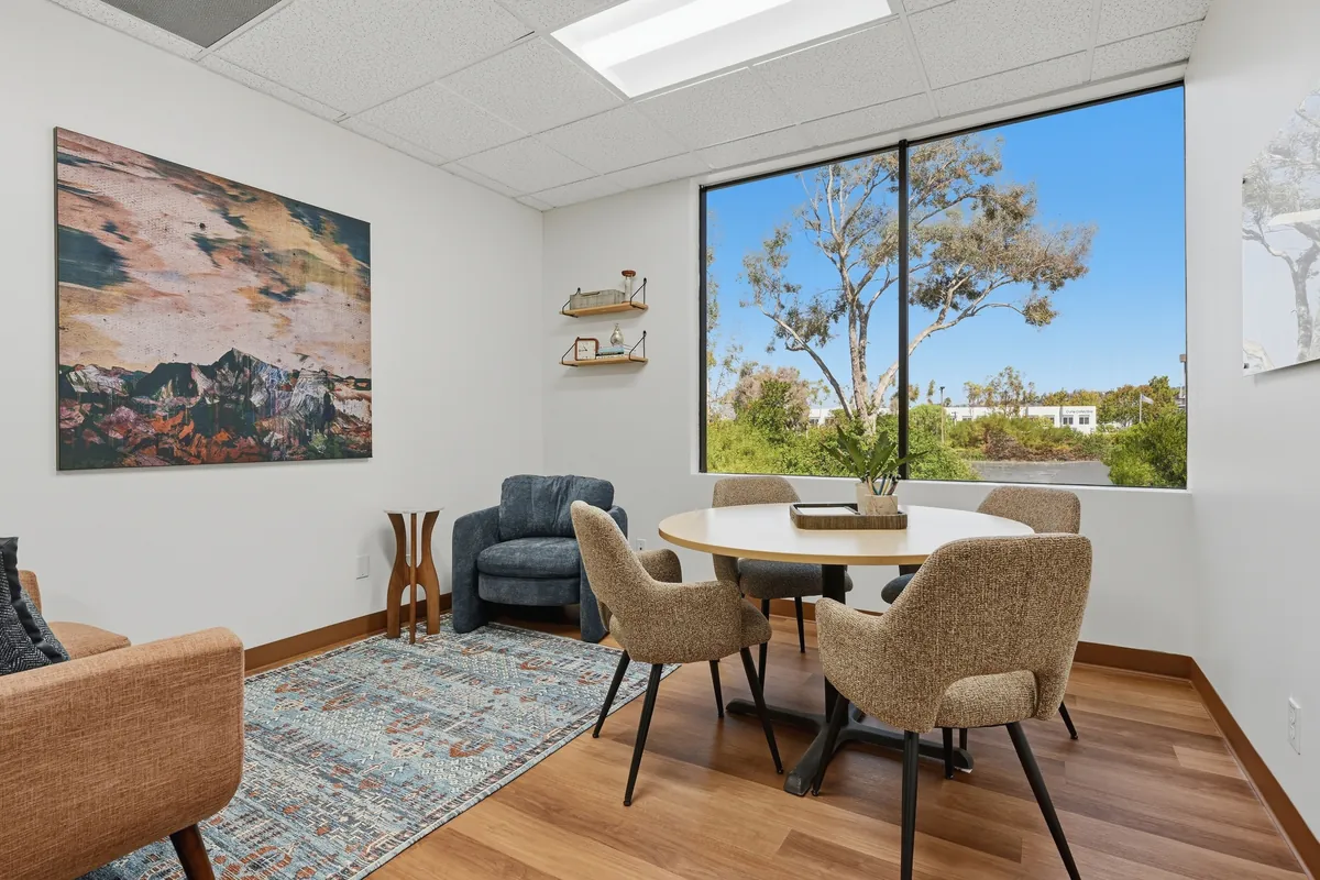 A small room with a round table, soft chairs and a window looking out over trees