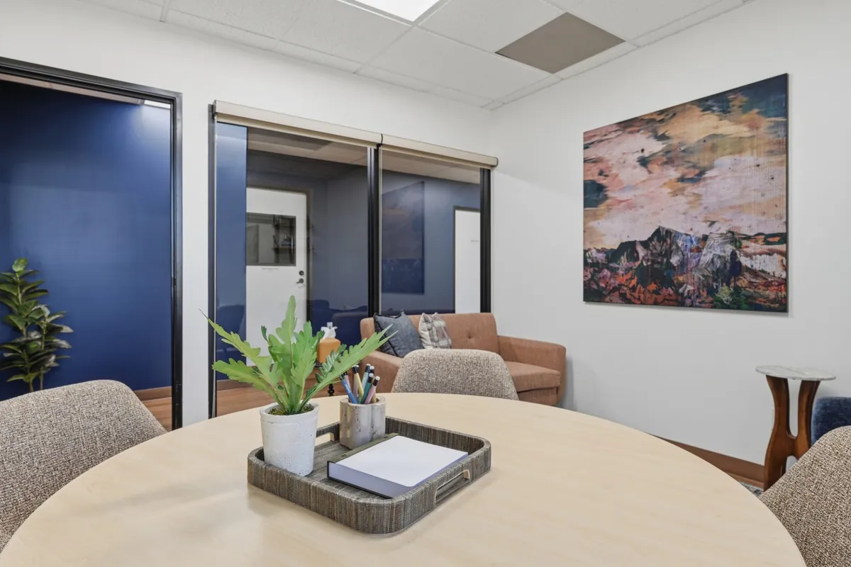 A round table with a tray of notepads and pens, looking through a glass wall into a deep blue group room