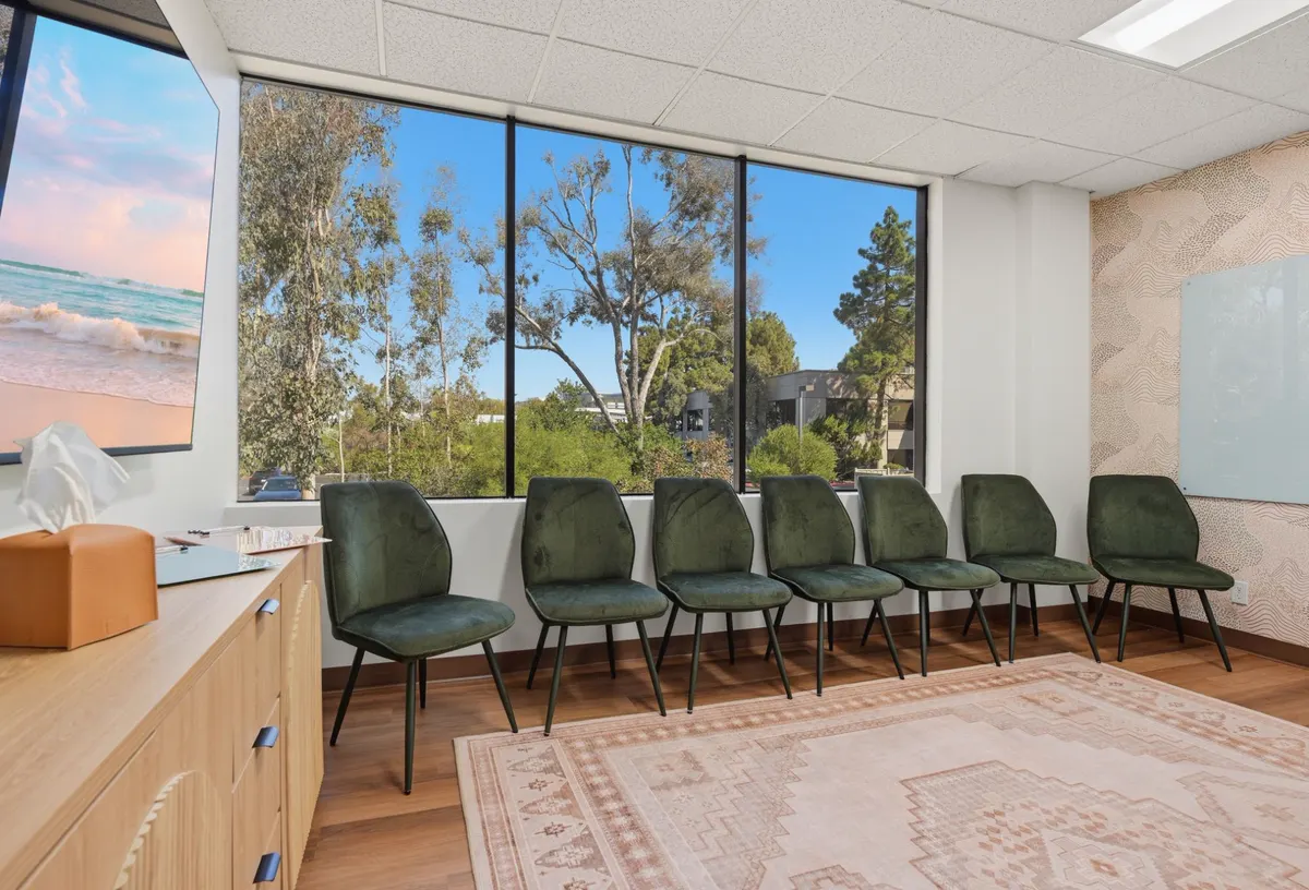 A group room with green upholstered chairs set along a wall of windows looking out over trees