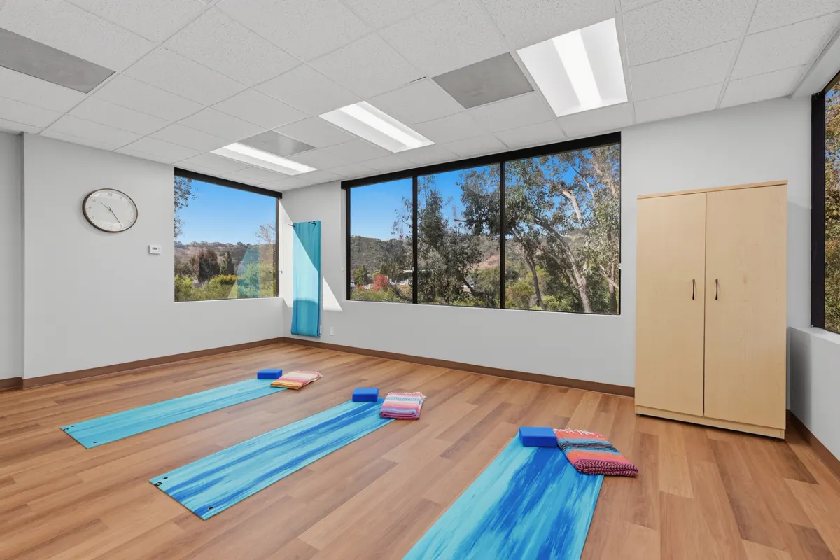 An open room with a wood floor, three yoga mats laid out with blocks and folded blankets, and large windows looking out to trees and hills
